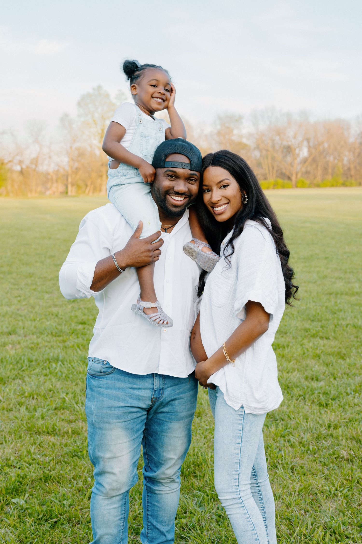 Family dressed in white and denim share joyful moment together in grassy field.