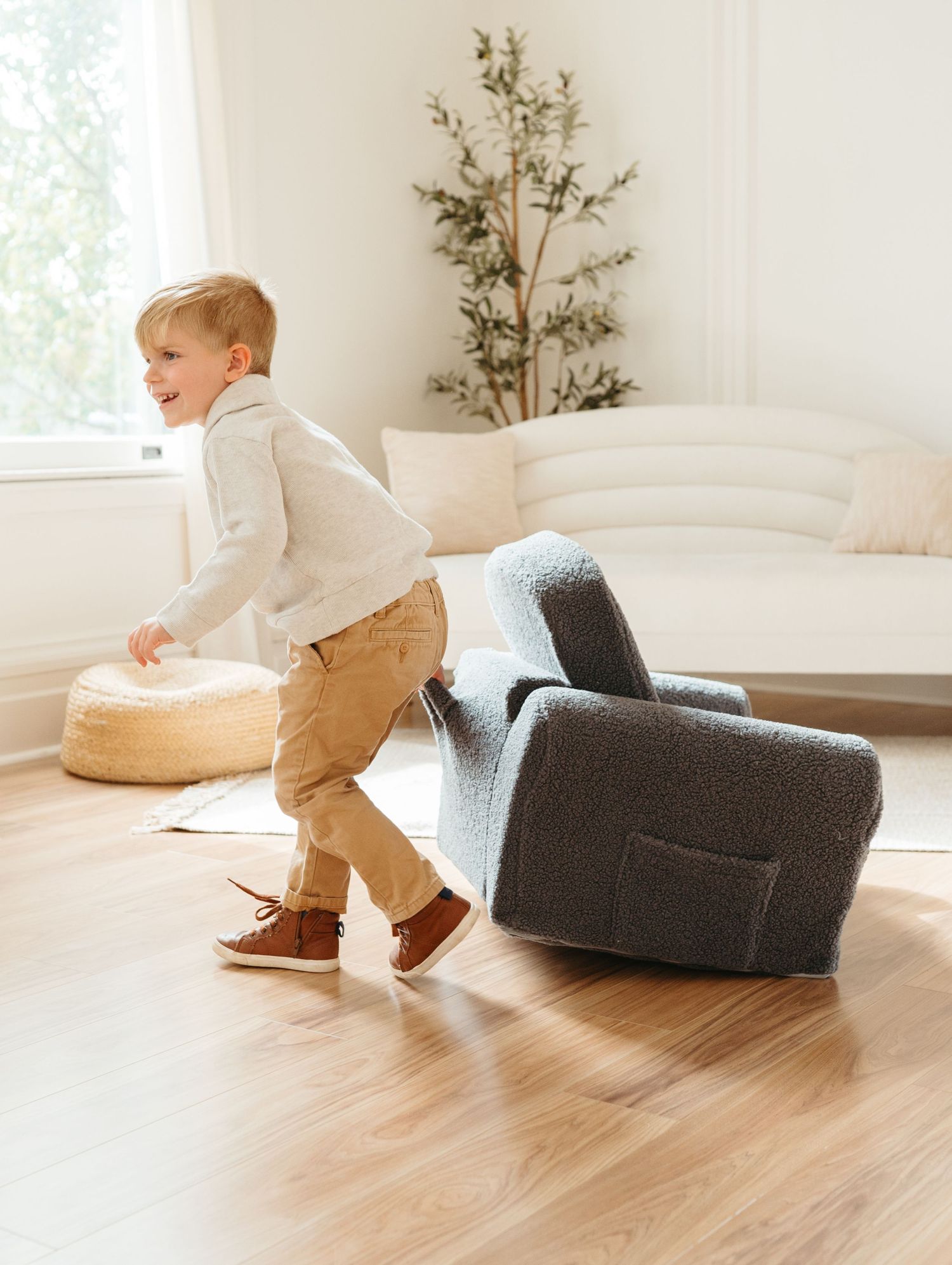 A child plays energetically with cushions in a minimalist white living room.