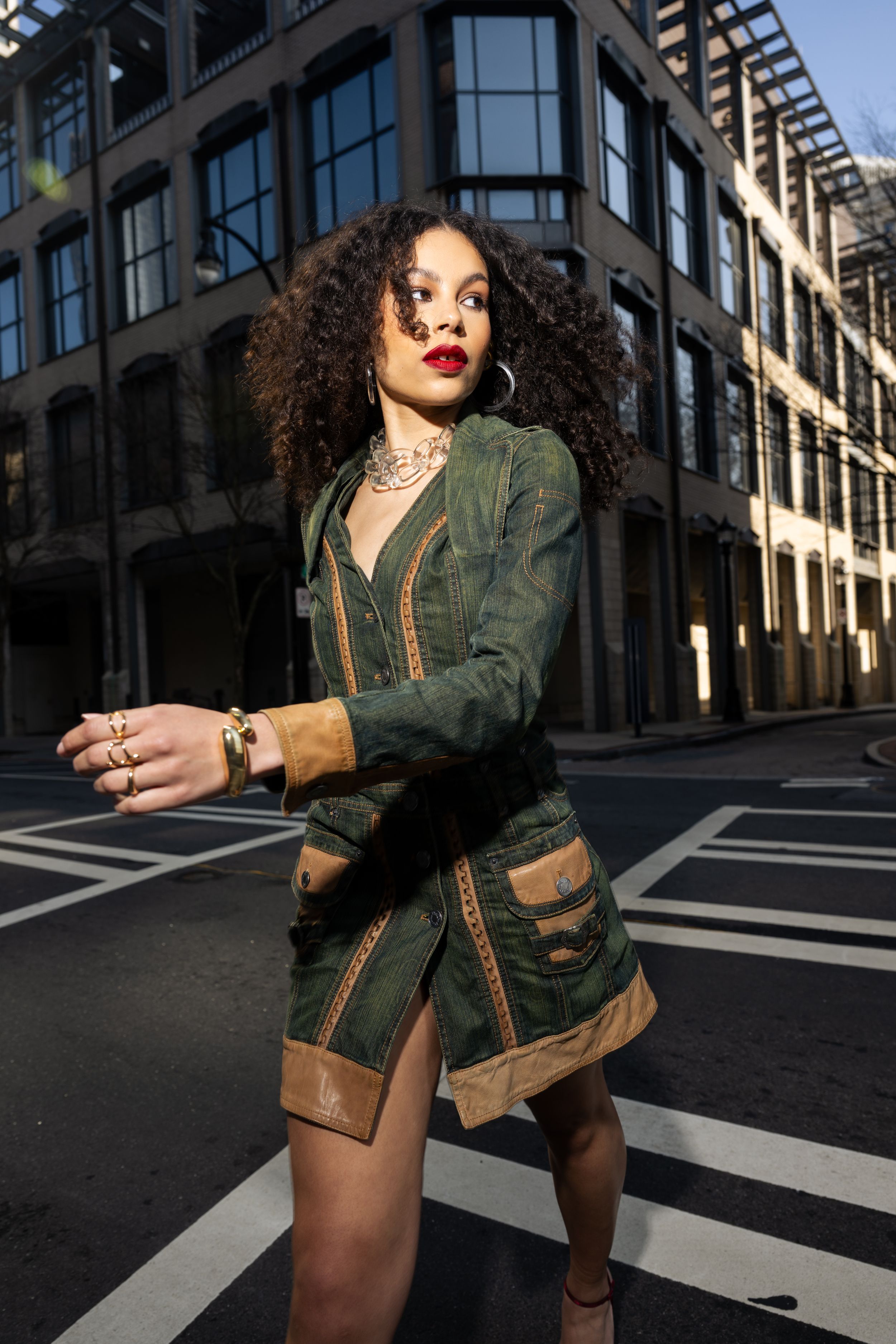 Fashion portrait in green jacket against urban architecture at sunset.