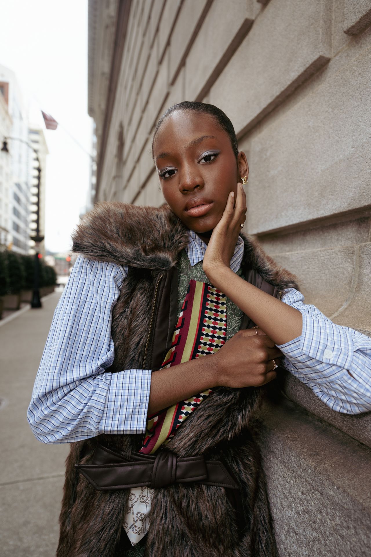 Winter fashion portrait featuring fur vest and striped shirt against urban wall.