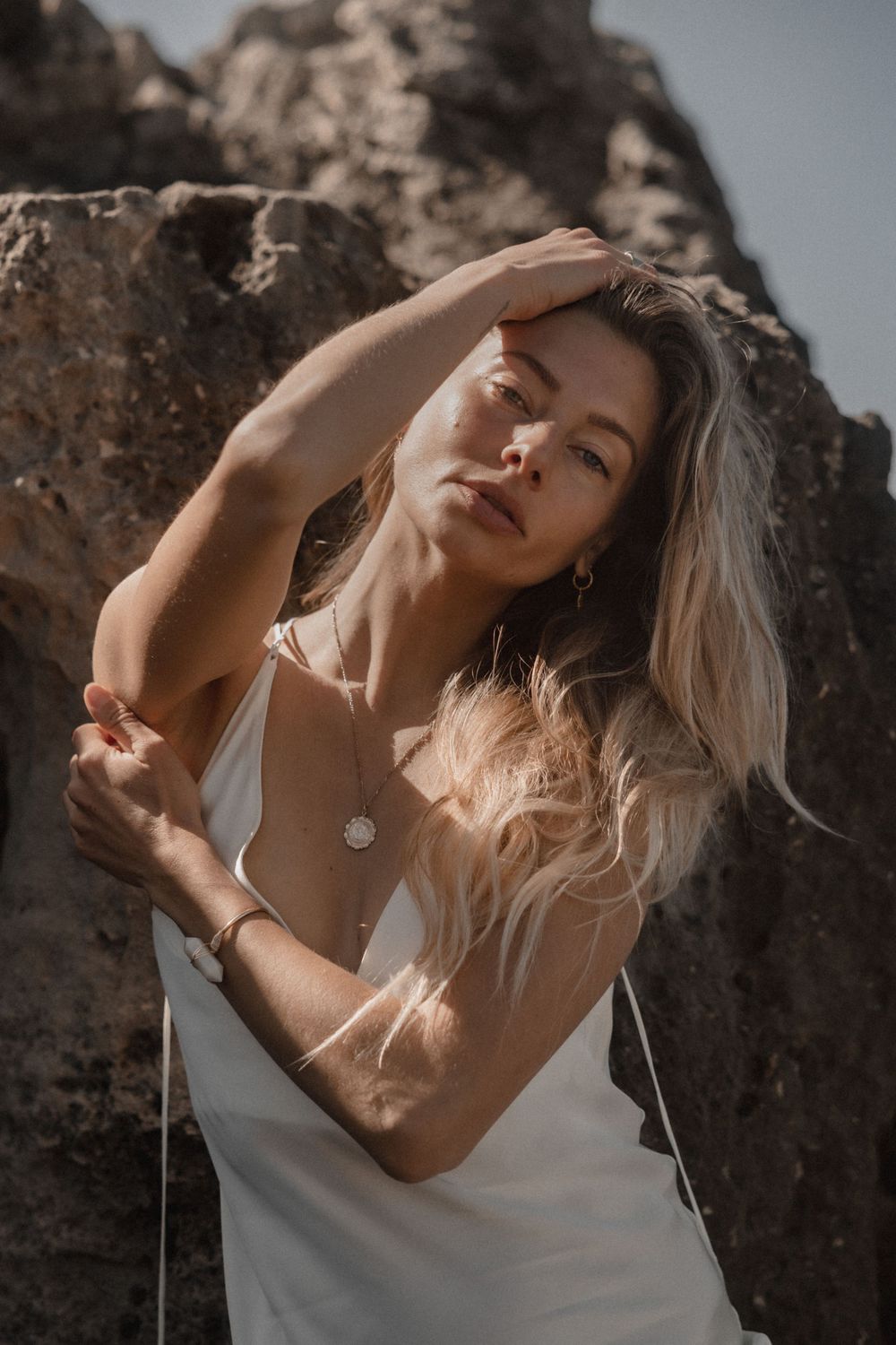 Sunlit portrait against rocky beach backdrop with white summer dress.