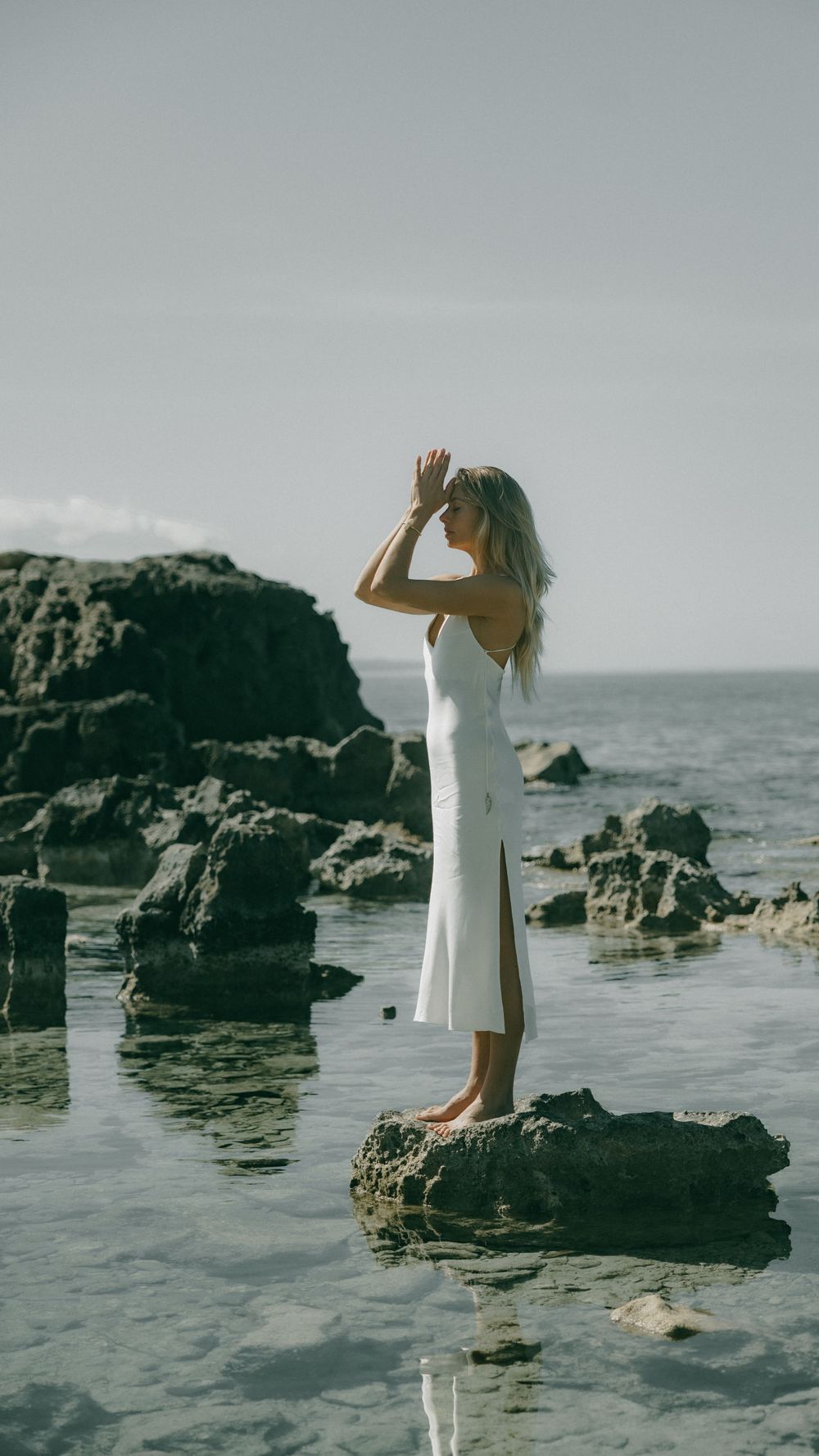 Ethereal beach photoshoot featuring white dress against dramatic coastal rocks.