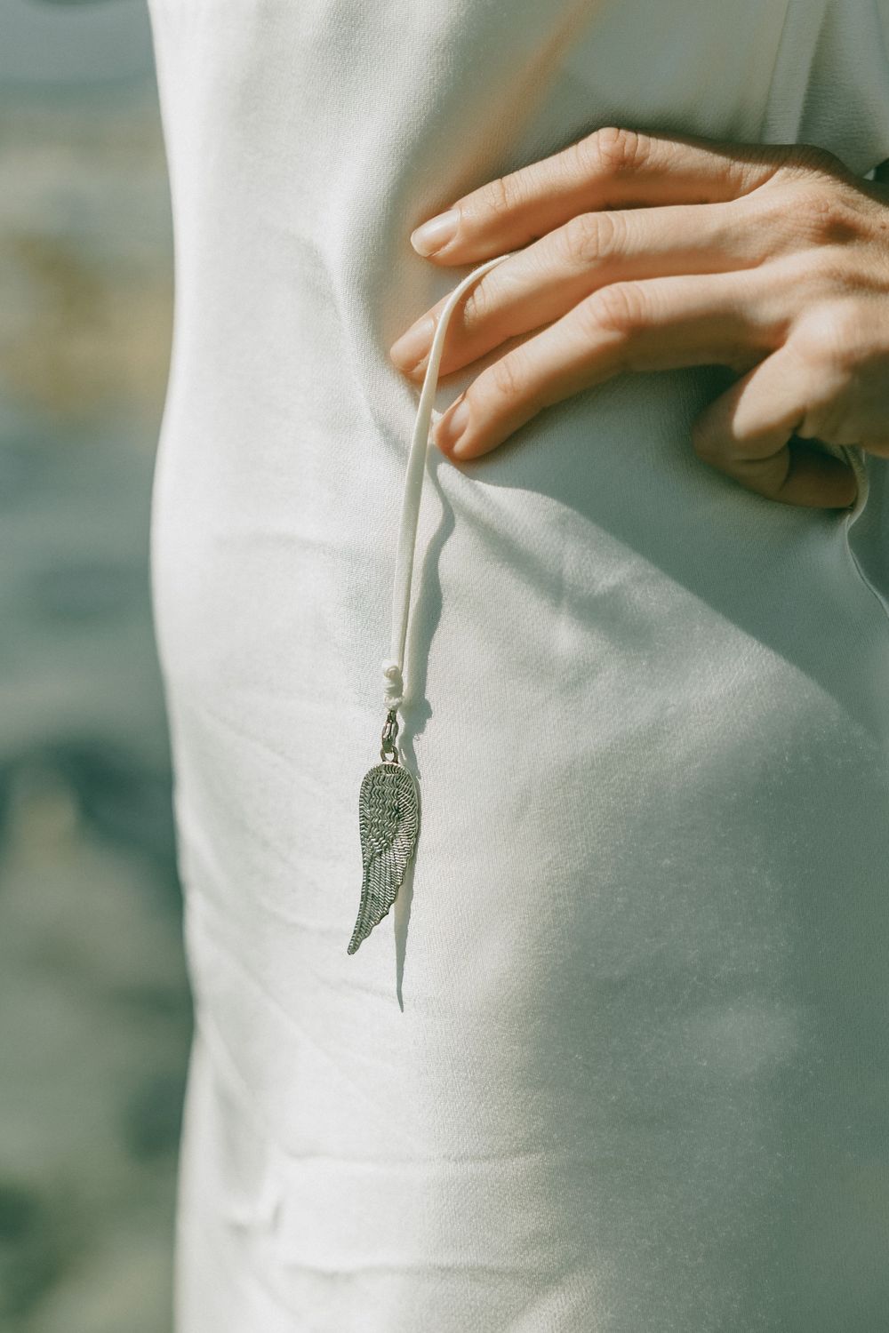 Detail shot of a hand holding a small silver key pendant against a white fabric background.