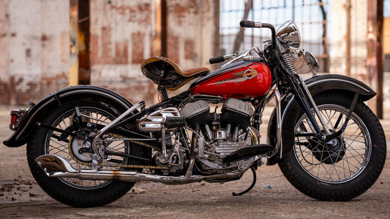 Classic vintage red and chrome motorcycle parked in industrial setting with rustic backdrop.