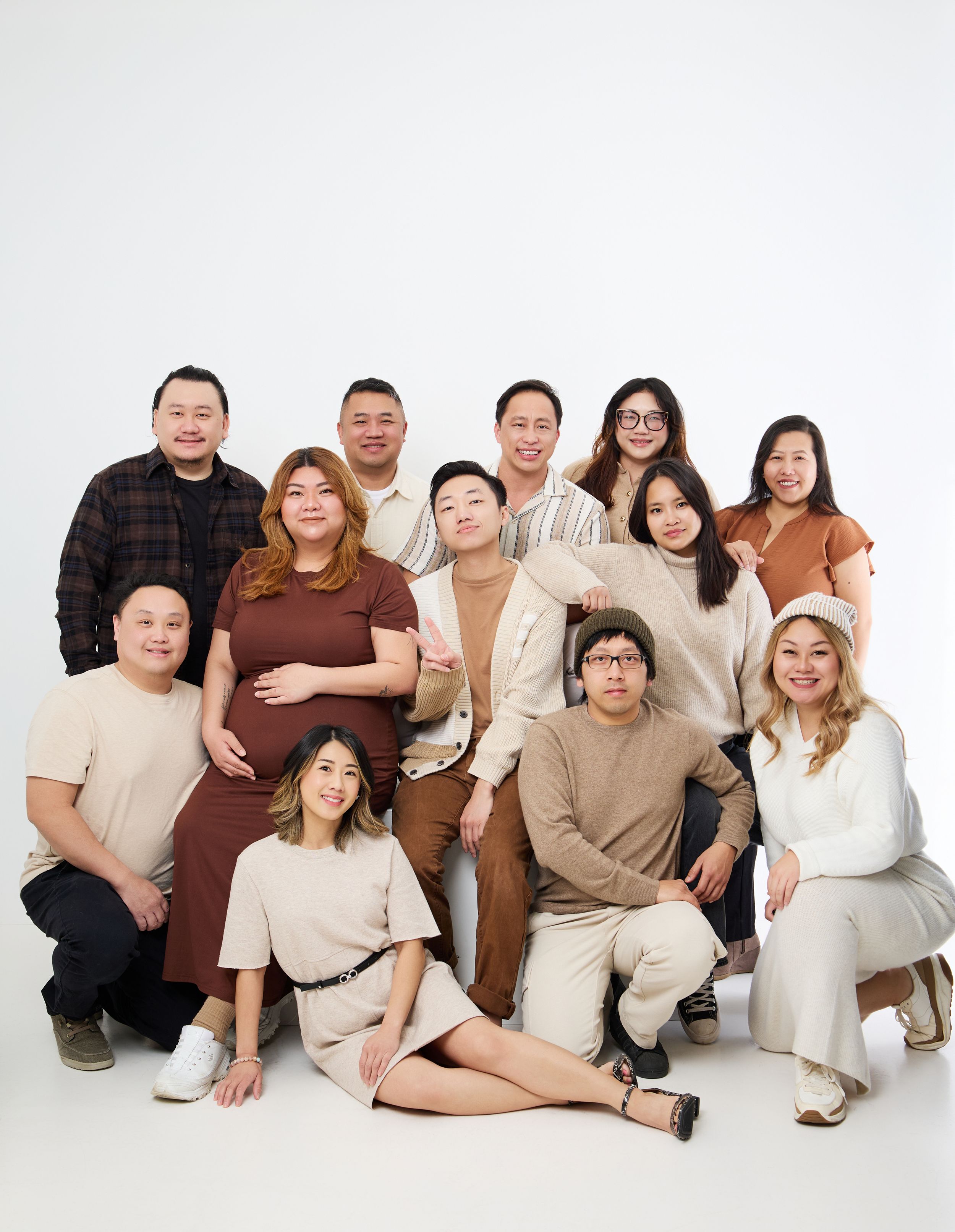 A group in neutral-colored casual outfits poses together for a studio portrait against a white background.