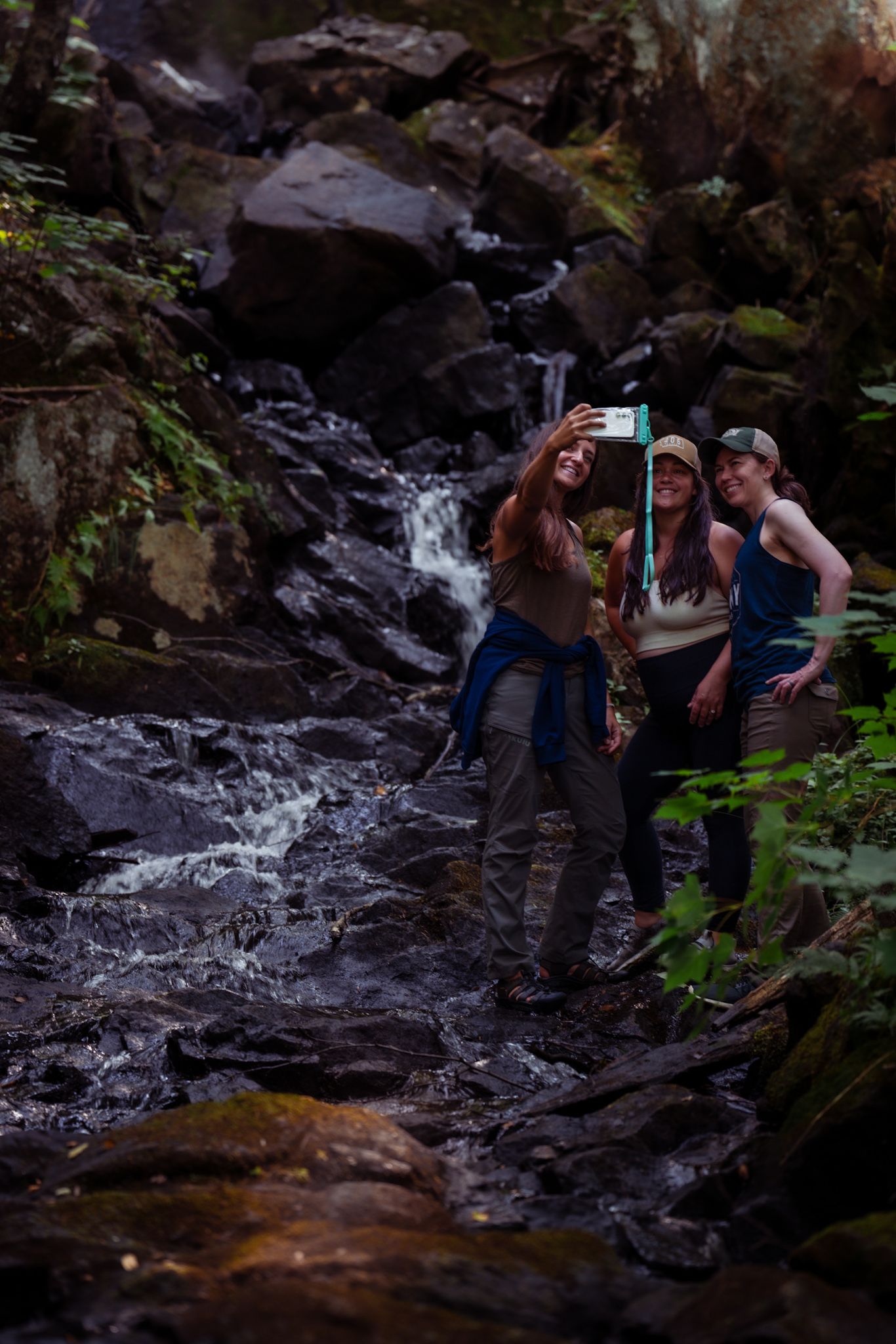 Hikers explore a scenic mountain waterfall trail surrounded by moss-covered rocks and flowing water.