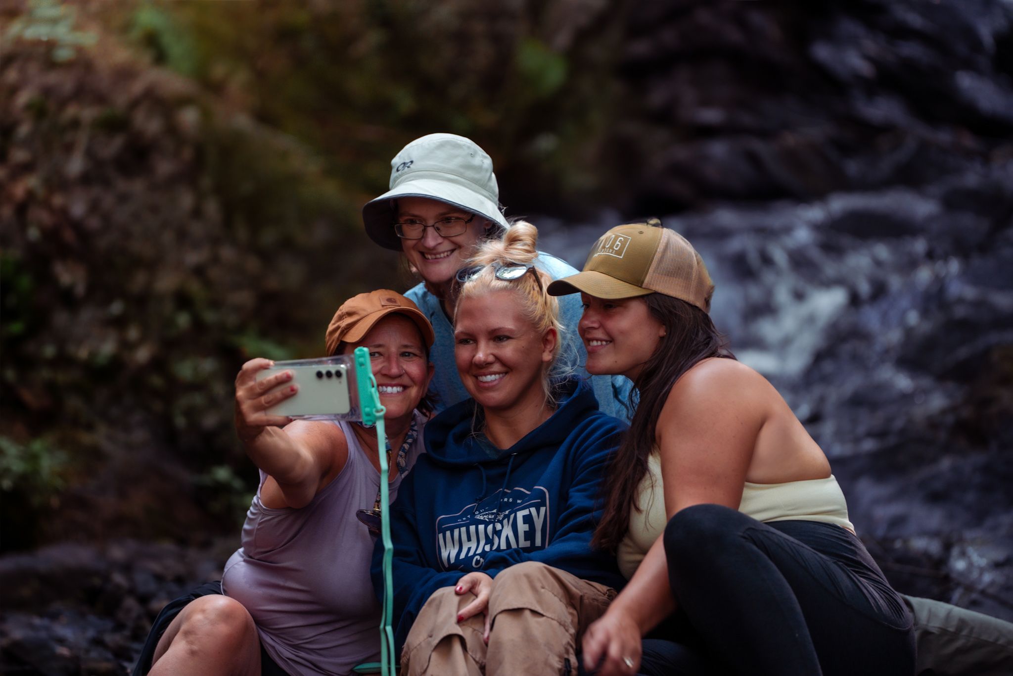A group of friends taking a selfie together while smiling and enjoying nature near a waterfall outdoors.