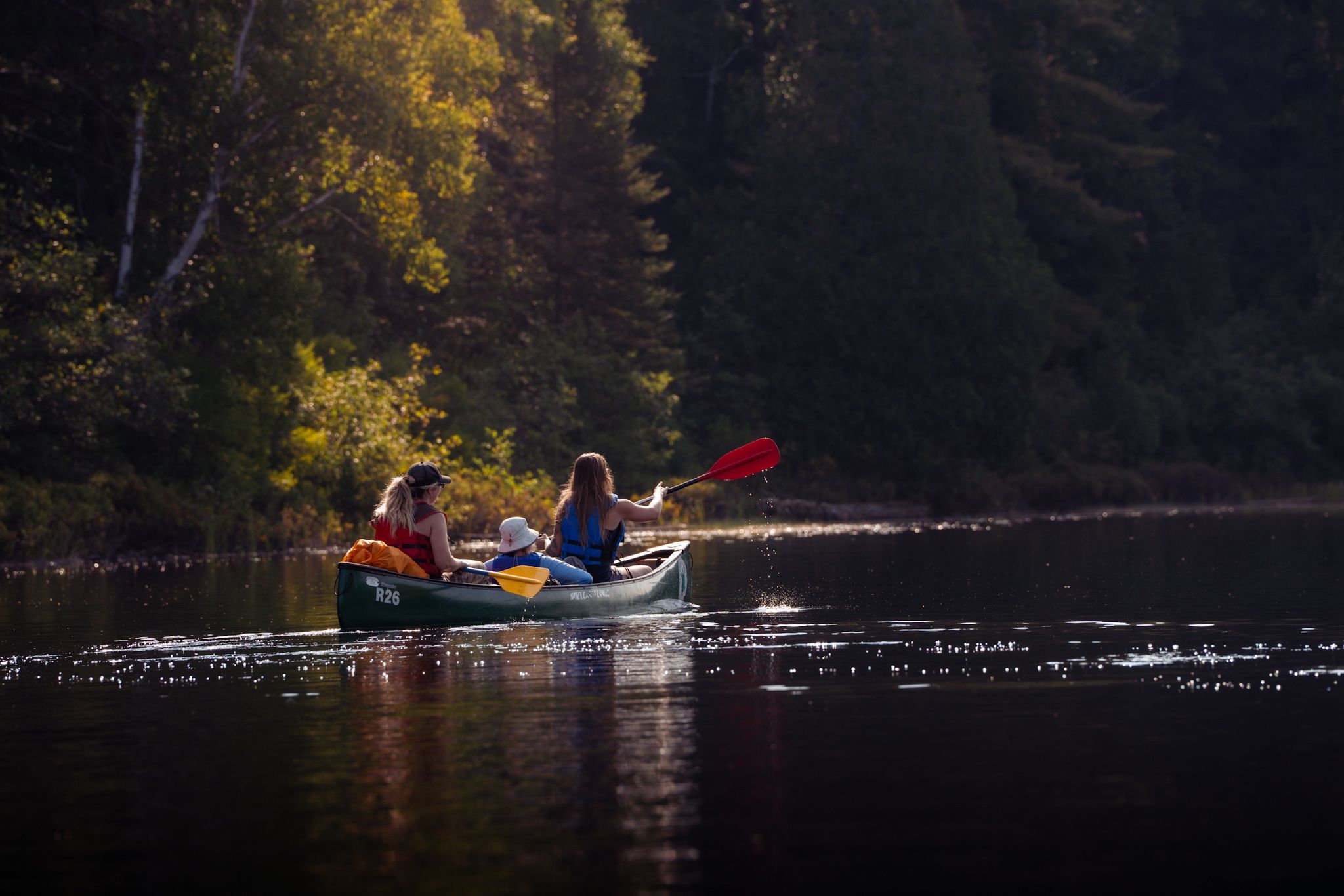 Two kayakers paddle across a serene lake during golden hour with autumn trees reflecting in the dark water.