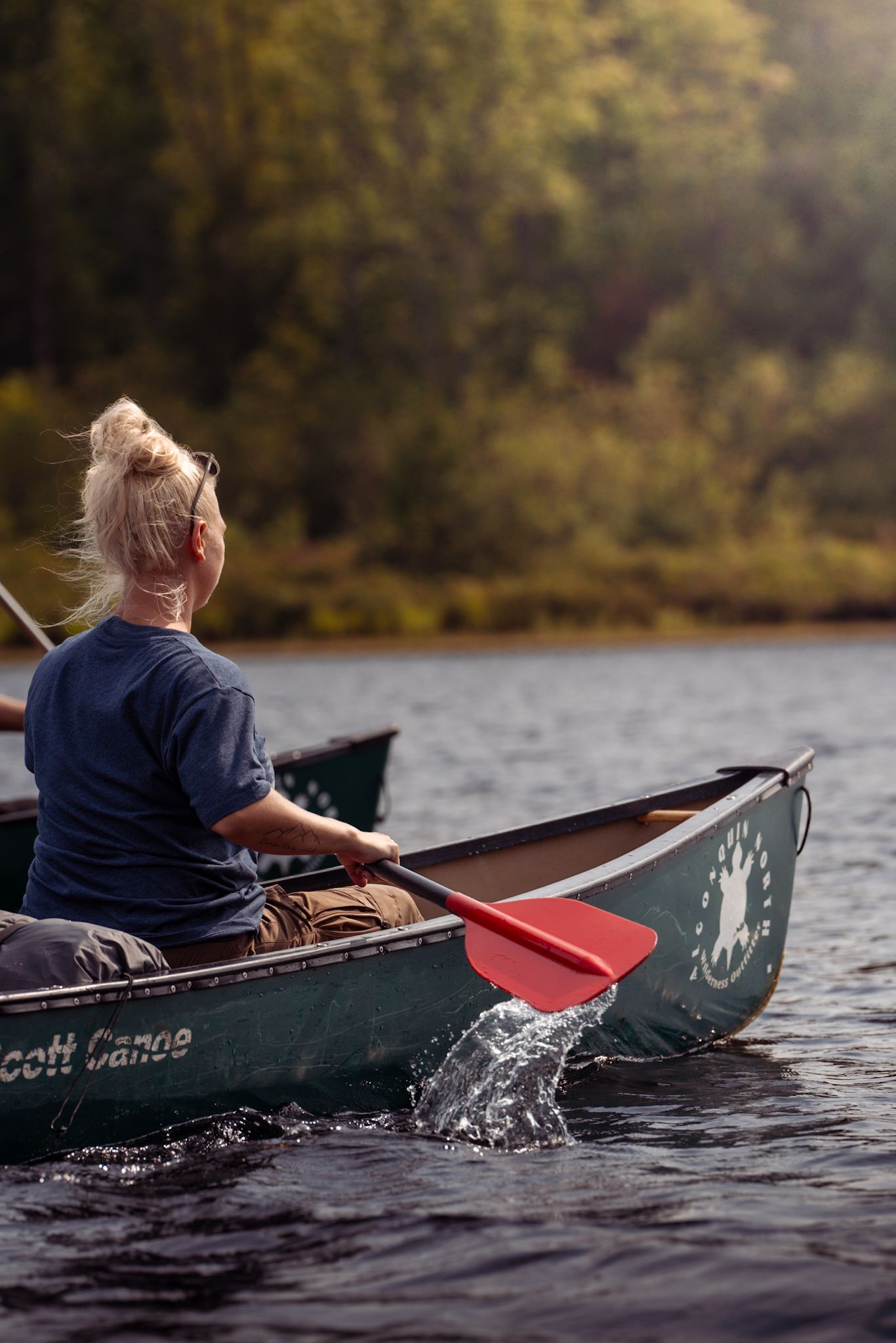 A person paddles a Scott canoe across a serene lake during golden hour, creating ripples in the calm water.