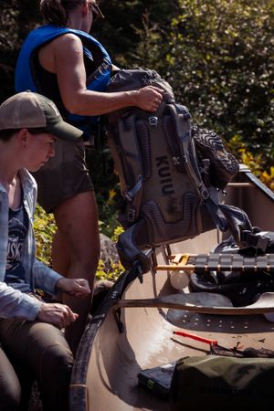 Outdoor adventurers preparing gear and equipment on a sunny day with backpacks and camping supplies.