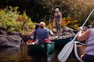 Outdoor adventurers navigate a green canoe between rocky outcrops on a serene lake during autumn.