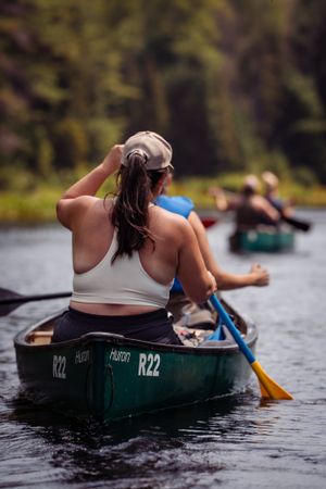 Person paddling a green canoe numbered R22 on a calm lake with other boats visible in the background.