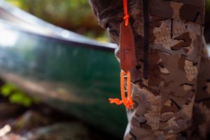 Orange tent rope secured to a tree trunk with camouflage bark pattern next to a green blurred background.