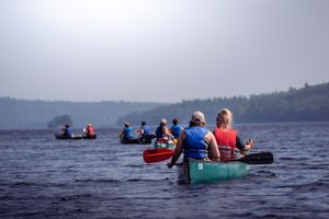A group of people canoeing on a serene lake with forested shoreline in the background during summer.
