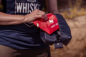 Someone's hands hold a red and navy outdoor gear bag while arranging or organizing its contents.
