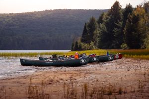 Black canoes rest on the shoreline of a scenic mountain lake surrounded by autumn trees and evergreen forest.