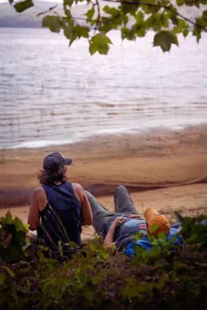 A person relaxes on a peaceful lakeside beach surrounded by maple leaves, enjoying the tranquil waterfront view.