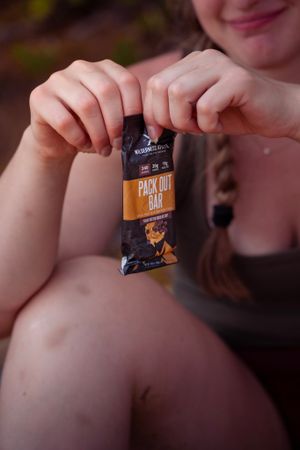 Hands holding a packet of Moonshot Pack Out BBQ flavored snacks against a blurred background.