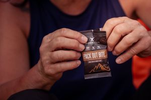 Hands hold an unopened pack of Jack Link's beef jerky against a dark background.