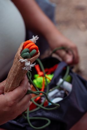 Close-up of hands holding wireless earbuds in a brown woven case with charging cables visible in the background.