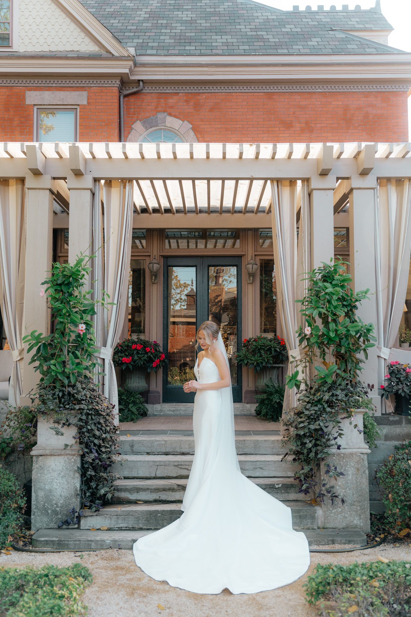 Beautiful bridal portrait at historic brick mansion entrance with white pergola, draping curtains and climbing greenery.