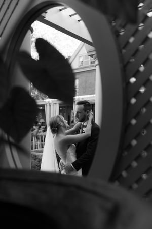 An artistic black and white wedding photo framed through an ornamental arch showing a tender moment.