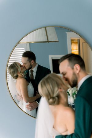 A romantic wedding moment captured in a round mirror reflection against a light blue wall.