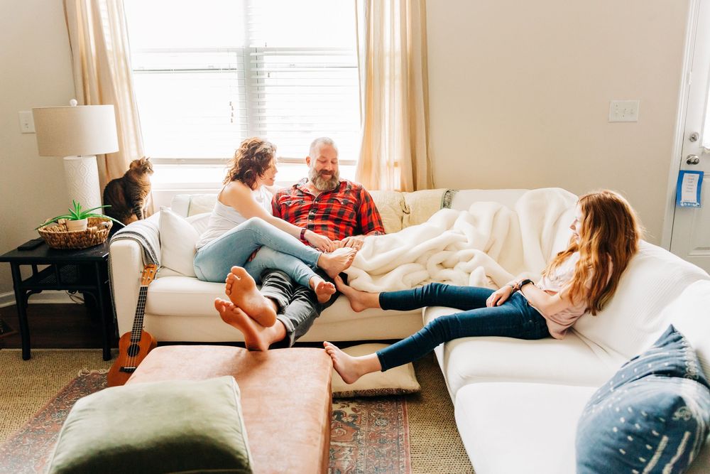 A family relaxes together on a comfortable white couch in a bright, sunlit living room.