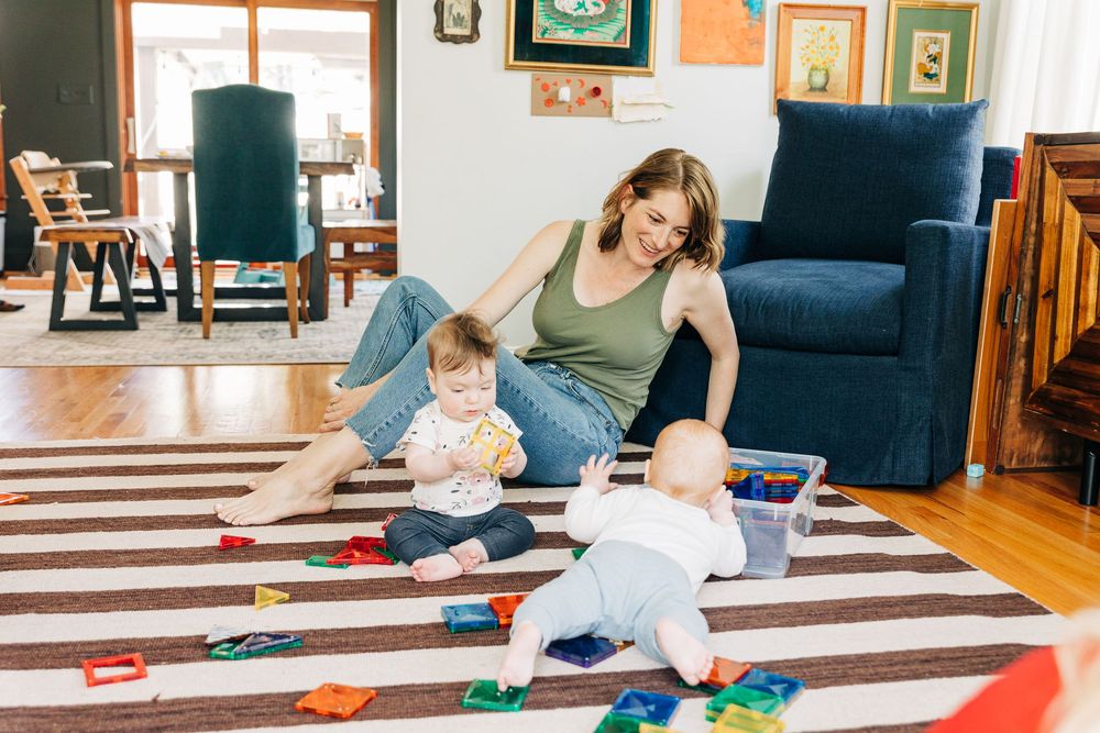 A mom plays on the floor with her twin babies. The rug is black and white.