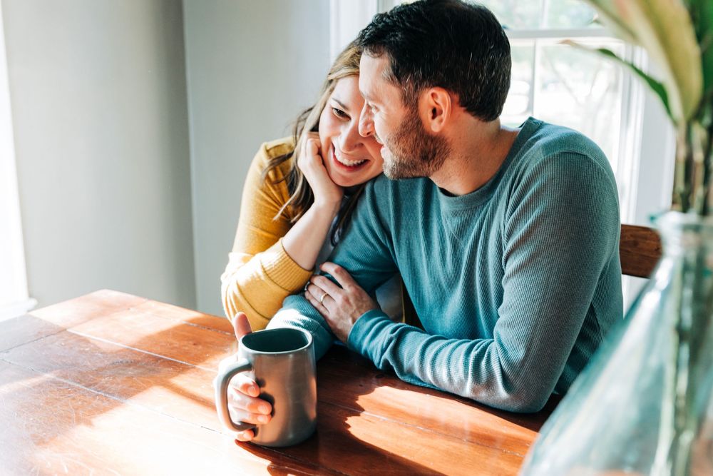 Two people having coffee and conversation at a wooden table in a bright, modern setting.
