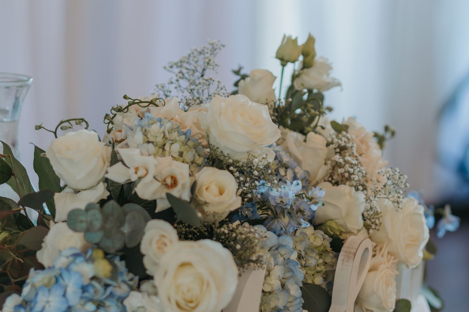 Elegant white and blue floral wedding bouquets with roses and delicate baby's breath arranged for a table setting at San Clemente Shores.