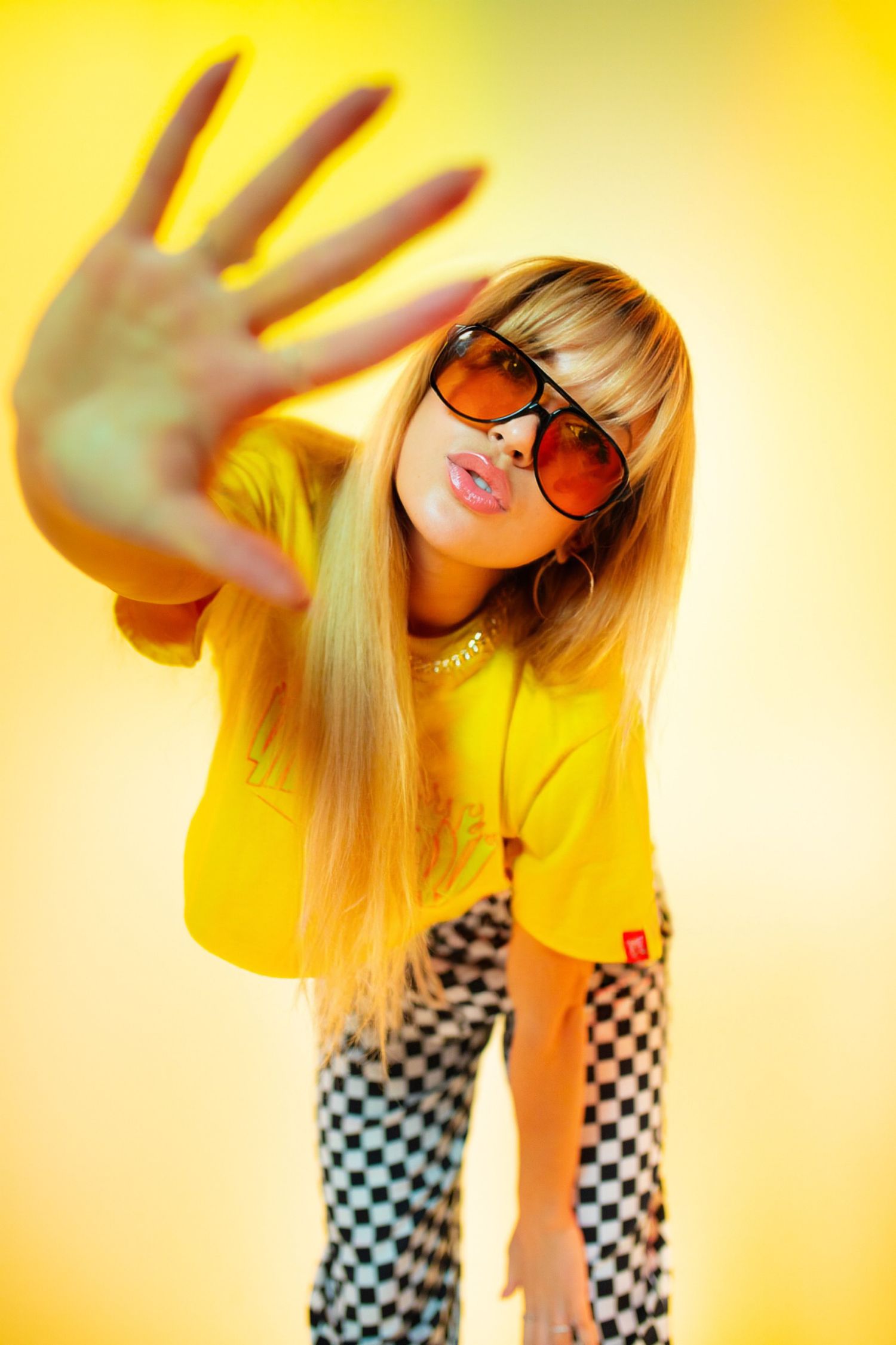 A figure in a yellow shirt and checkered pants poses dynamically against a bright yellow background.