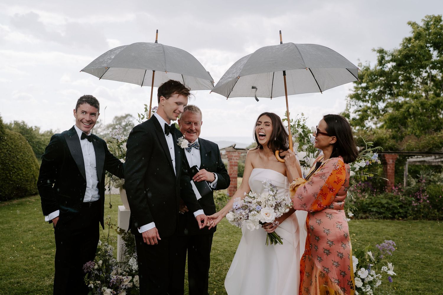 bride and groom sheltering underneath umbrellas during a rain shower during the ceremony at dewsall court in herefordshire