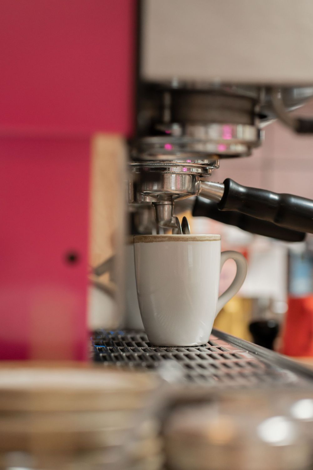 Close-up view of an espresso cup under a coffee machine portafilter on a metal grate surface.