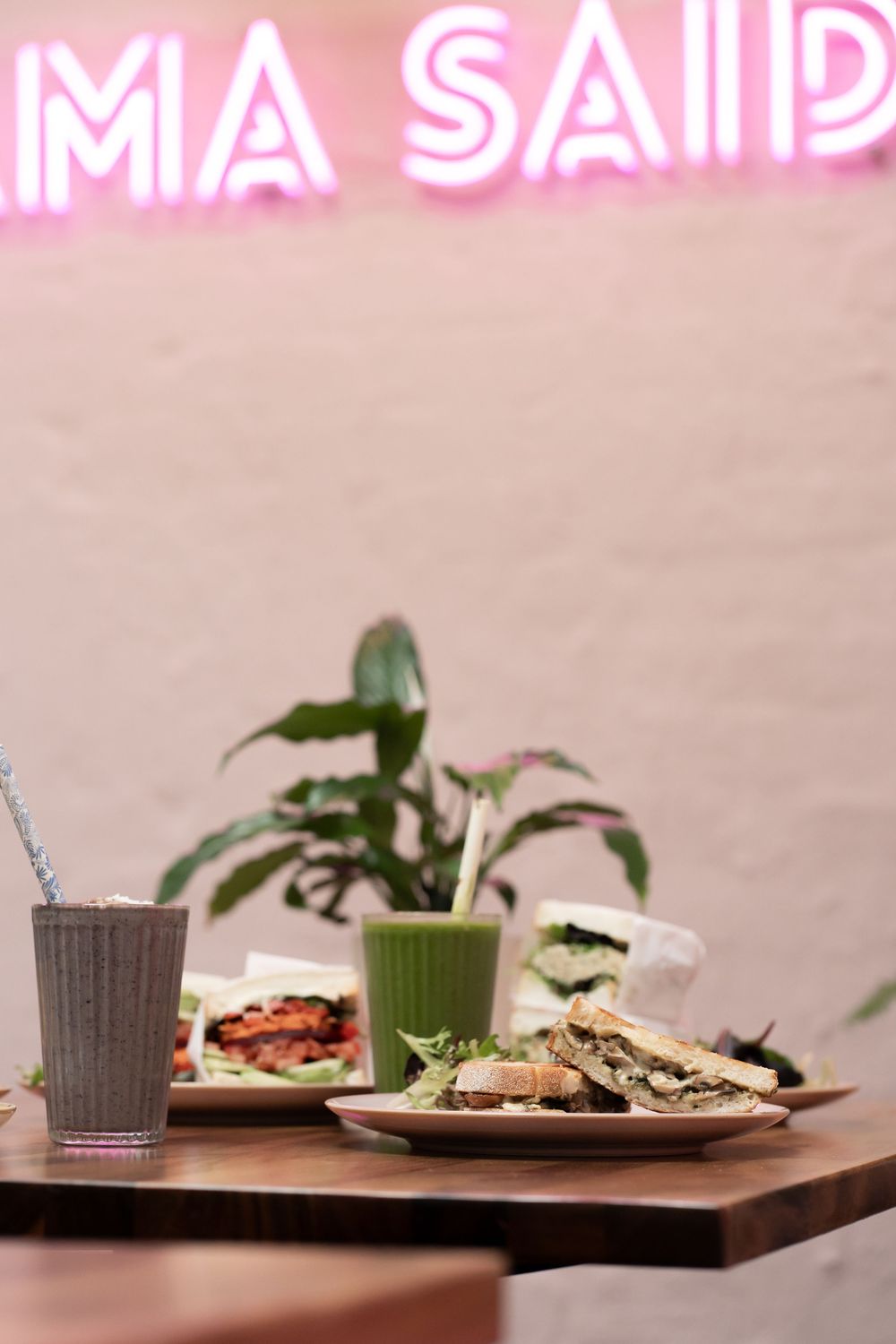 Restaurant table setting with colorful drinks and plates against a pink neon sign backdrop.