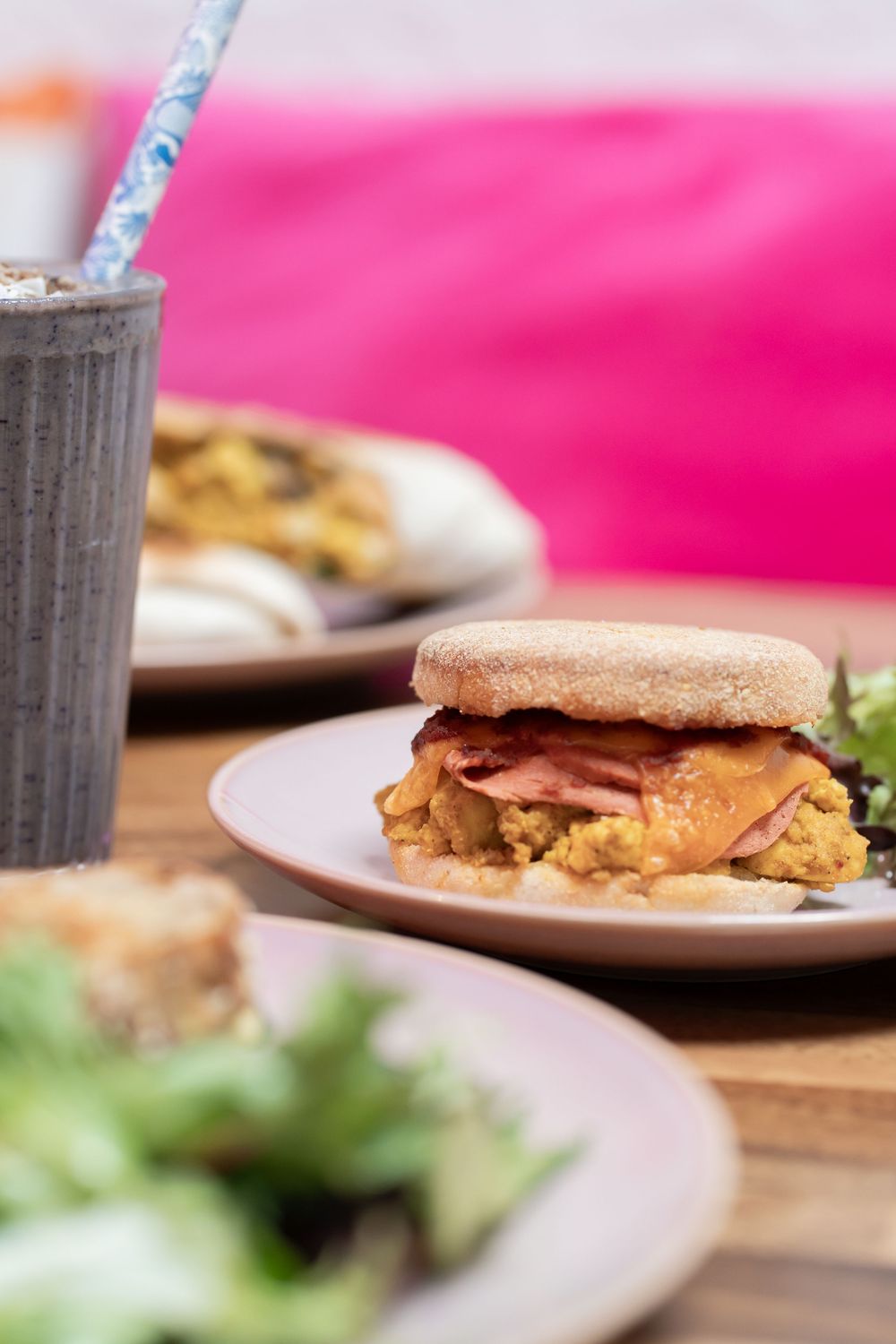 Sandwiches and milkshakes arranged on wooden tables with pink background accents.