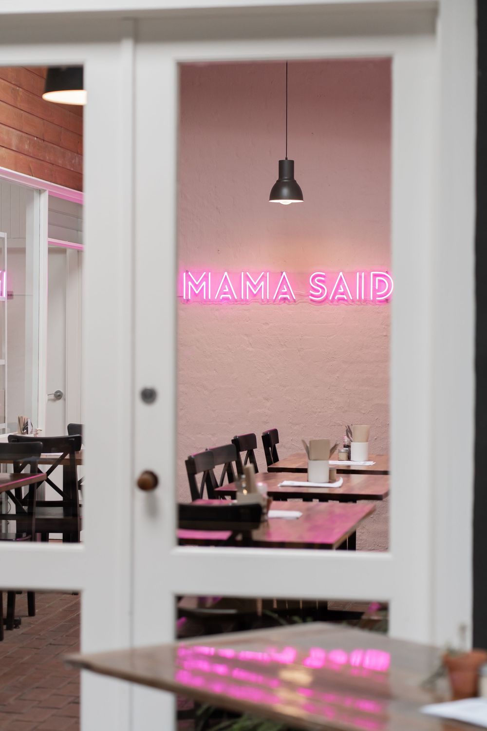 Modern restaurant interior with pink neon 'MAMA SAID' sign and dark wooden furniture.
