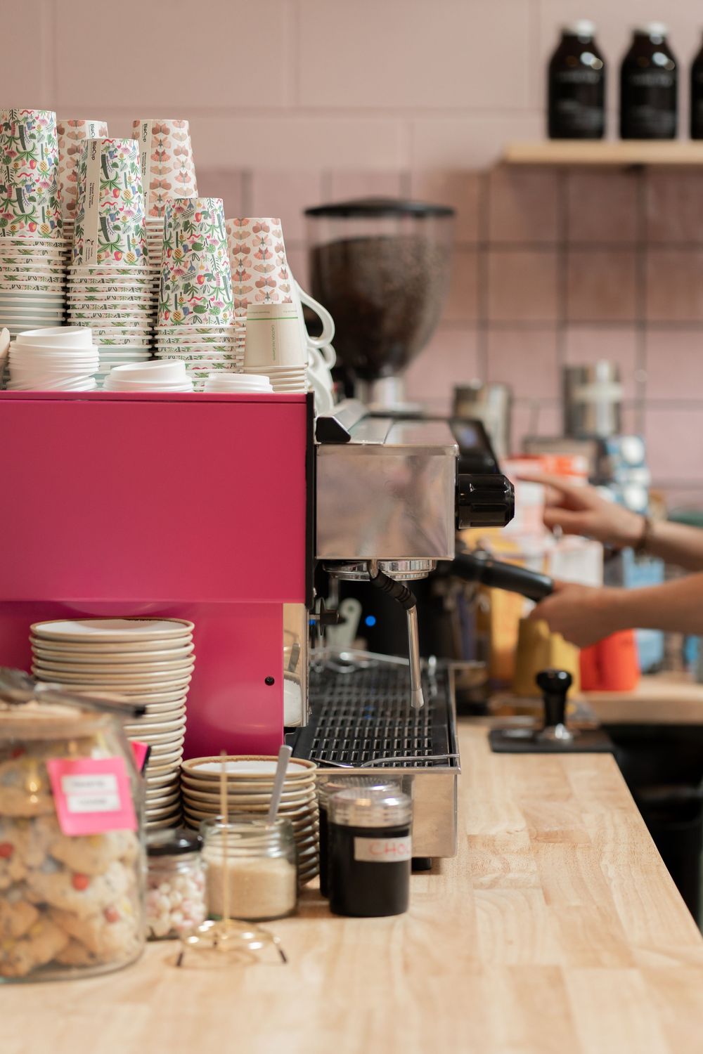 Stacks of white plates and disposable cups arranged on a wooden counter in a cafe kitchen setting.