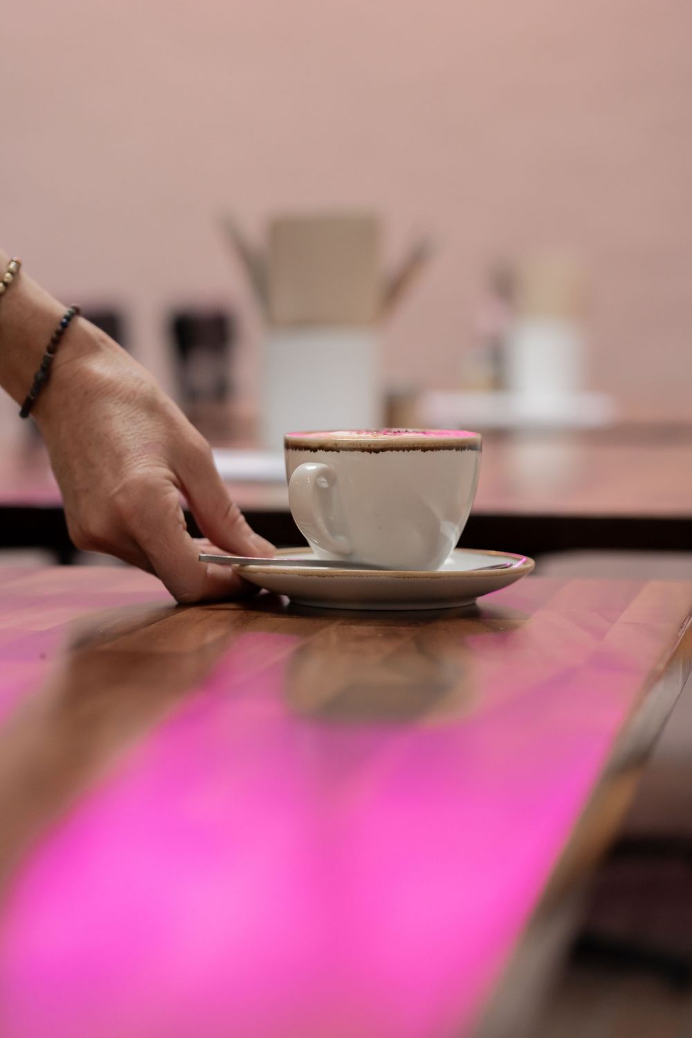 A white coffee cup sits on a table with a pink glowing light effect in the background.