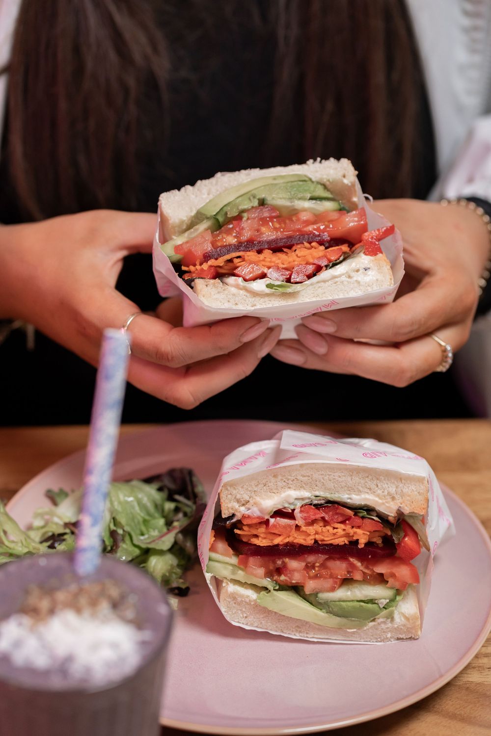 Close-up of a sandwich filled with bacon, tomato, and lettuce on a pink plate with a drink.