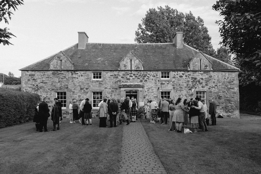 A group of people gathered outside historic stone buildings during what appears to be a social event or gathering.