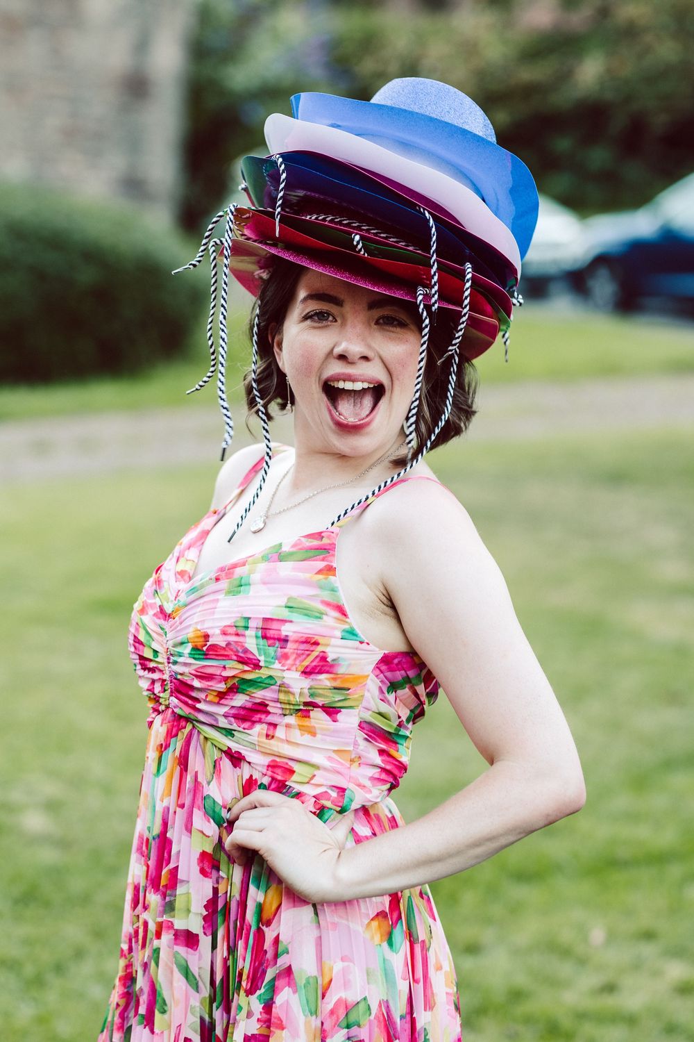 A person in a floral summer dress and red and blue hat poses playfully outdoors in a series of candid shots.