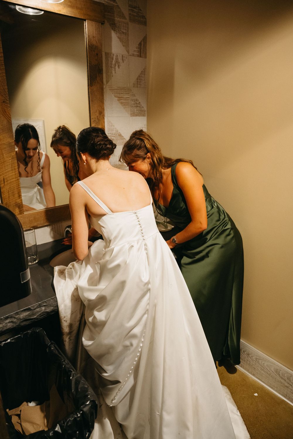 People in formal attire prepare in a dimly lit room with one wearing a flowing white dress.