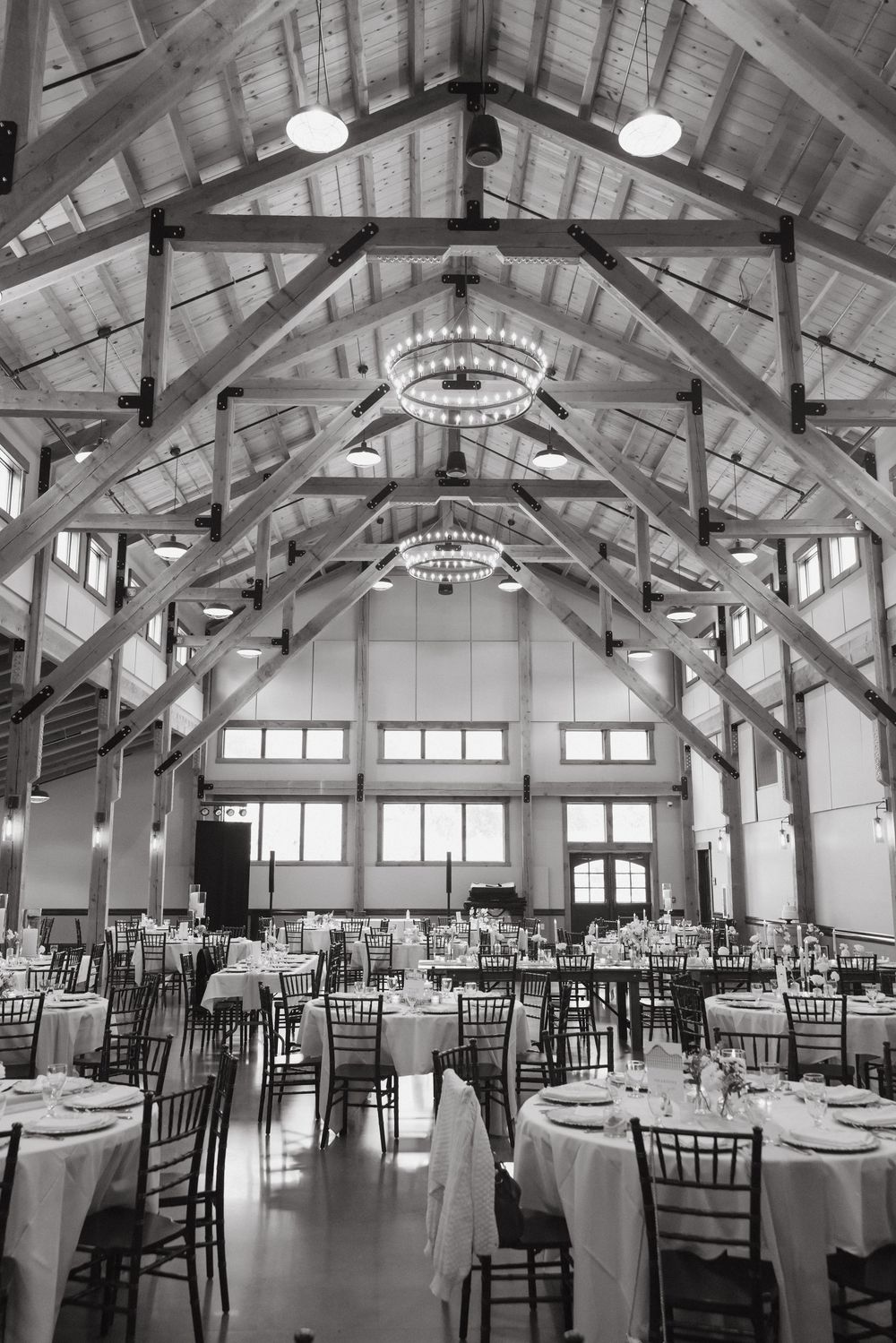 Rustic wedding reception venue with exposed wooden beams, chandeliers and white table settings.