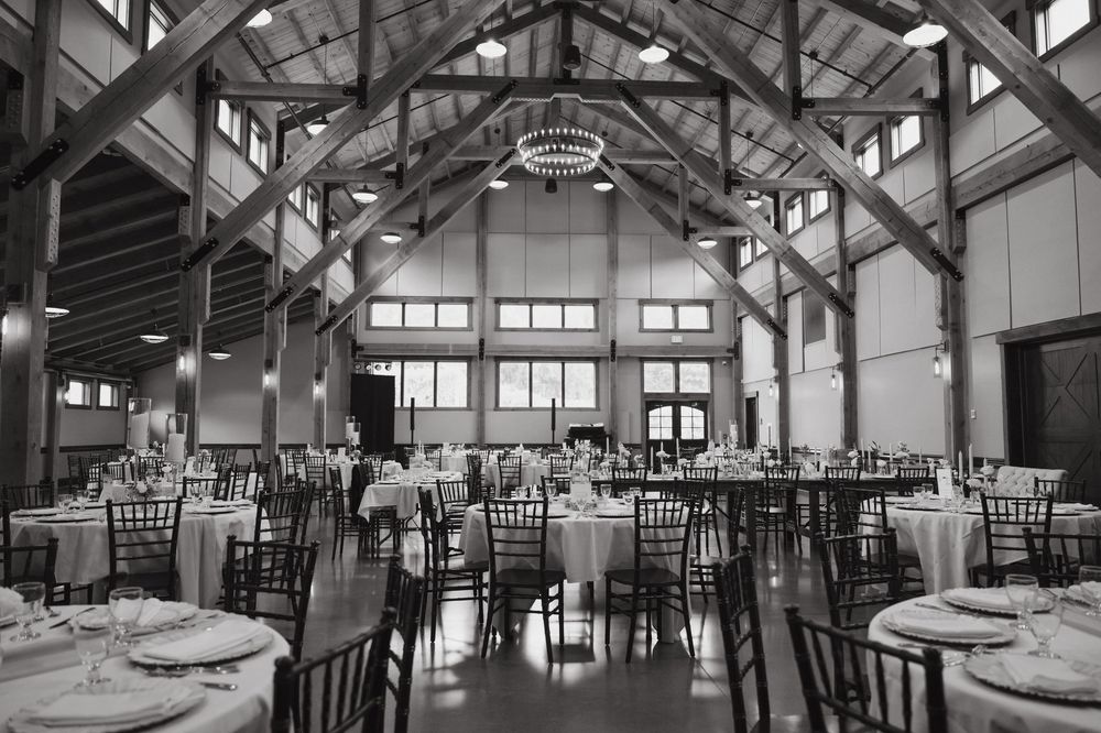 A panoramic black and white view of an elegant wedding reception venue with exposed beams and round dining tables.