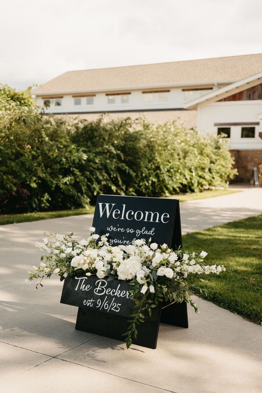 Black chalkboard welcome signs decorated with white flowers and greenery displayed on a concrete walkway.