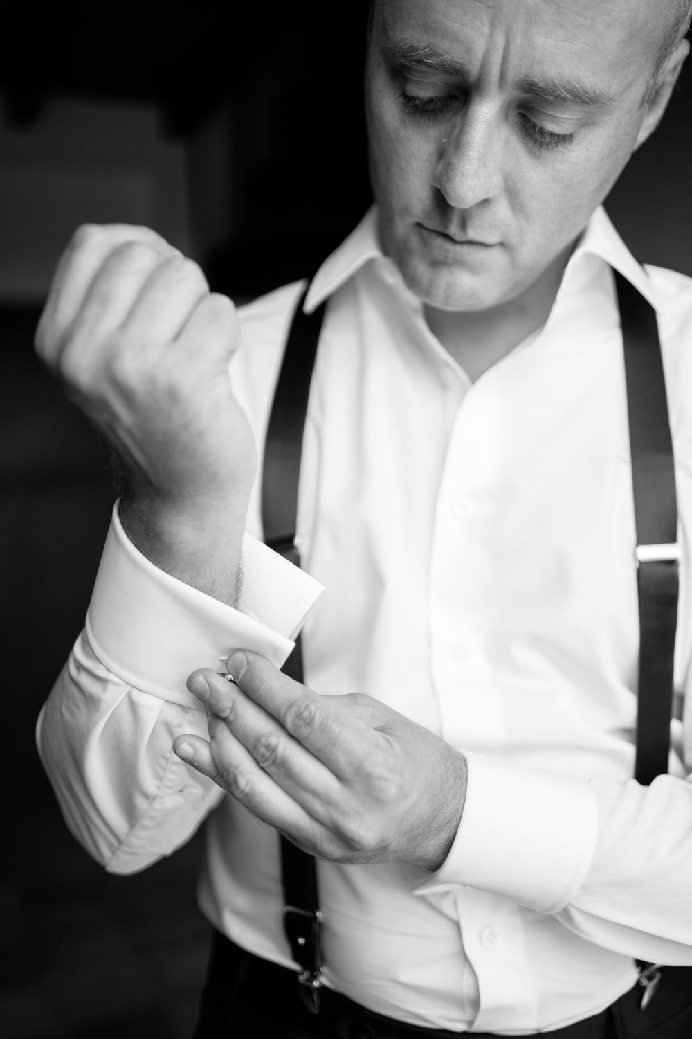 Black and white sequence showing hands adjusting white dress shirt cuffs and suspenders.