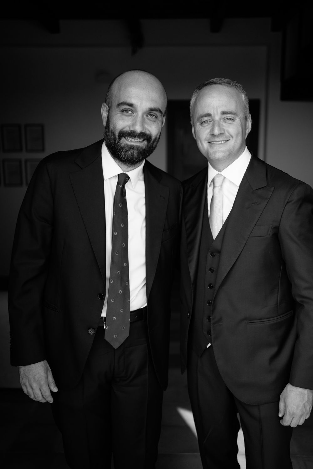 Two men in black suits and ties stand together smiling in a black and white photograph.