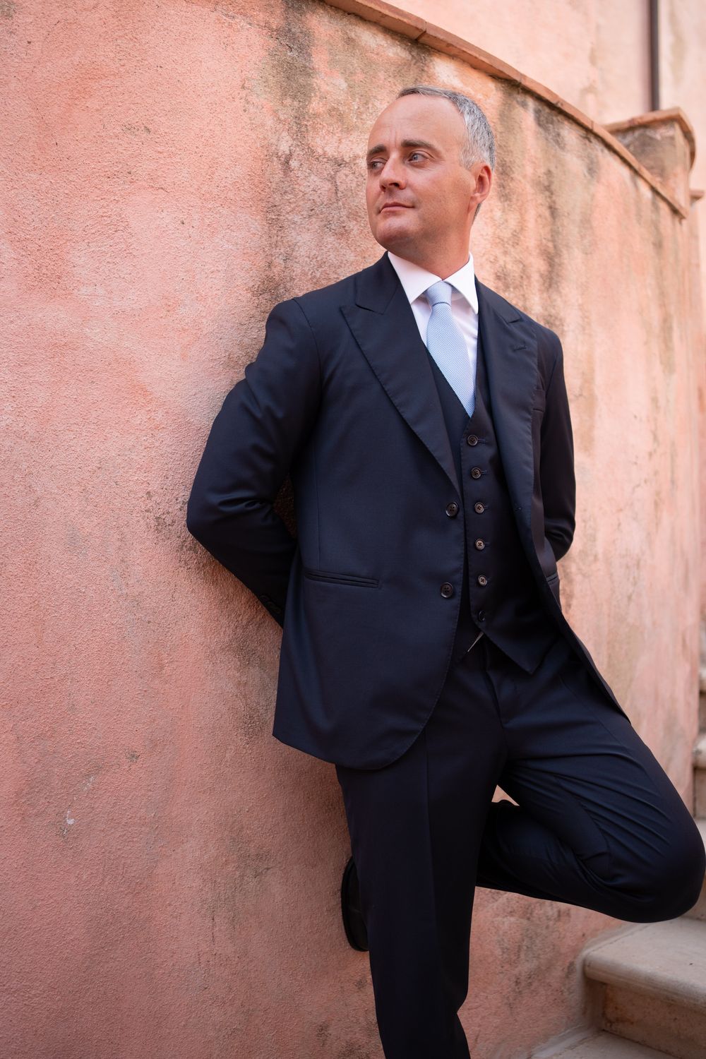 A person in a dark suit poses against a pink wall in multiple artistic shots.