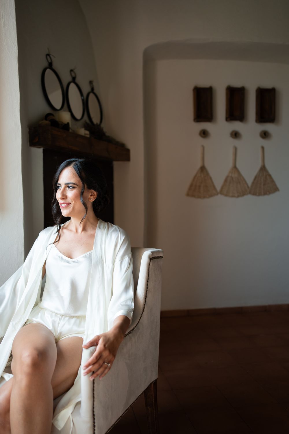 Woman in white dress sitting by a window in an elegant indoor setting.
